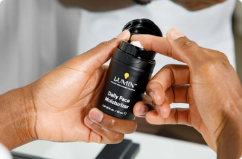 Lumin Daily Face Moisturizer with SPF 21 in a black bottle held by two hands, skincare product for men