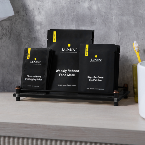 Black charcoal peeling, weekly reboot face mask, and eye de-gone eye patches skincare products on black rack with grey concrete wall background.