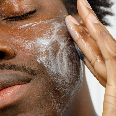 Close-up of man applying creamy facial cleanser on dark skin with hand, emphasizing skincare routine and moisturizing product usage.