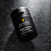 Lumin Instant Redness Corrector black skincare bottle on textured dark surface for men’s skincare.