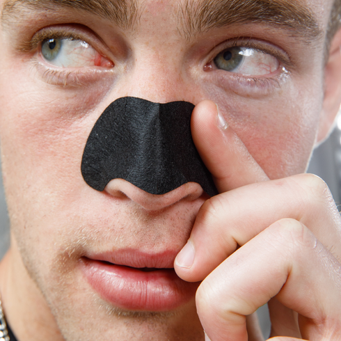 Close-up of man applying black charcoal nose strip for blackhead removal and skincare treatment