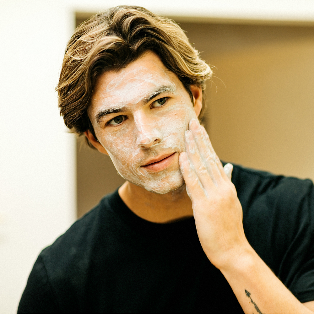 Young man applying foaming facial cleanser in bathroom, skincare routine for healthy and clear skin care, grooming.