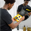 Man holding open black and yellow grooming kit box with black and white geometric-shaped soaps near bathroom sink and mirror.