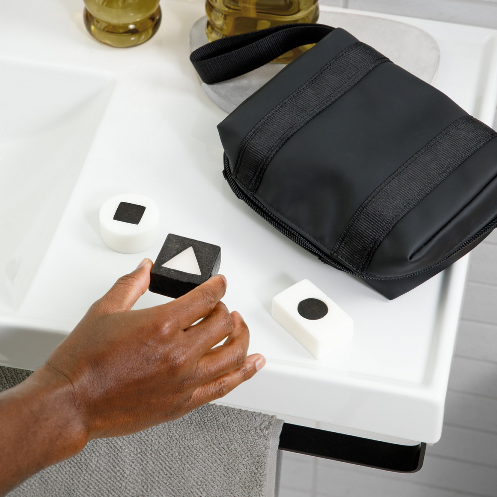 Left hand reaching for black and white sensory blocks with shapes on white surface next to black pouch and towel